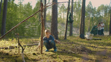 family-trip-in-picturesque-forest-at-summer-married-couple-is-pitching-tent-and-little-boy-is-playing